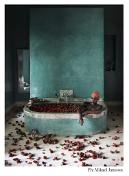 Black woman with orange swim cap sitting in a teal bathtub filled with red rose petals styled by Phyllis Posnick