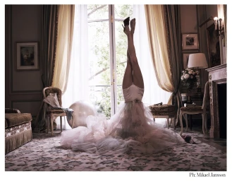 A person upside down on a patterned rug in a classic room wearing a voluminous tulle skirt and high heels with legs pointing vertically.