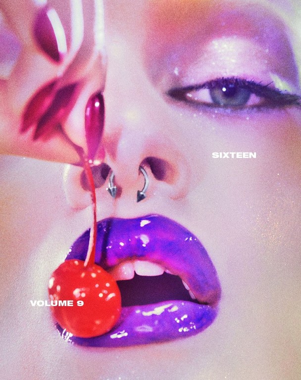 Close-up studio shot of a person with shiny makeup, purple lipstick, nose piercings, and a bright red cherry near their mouth.