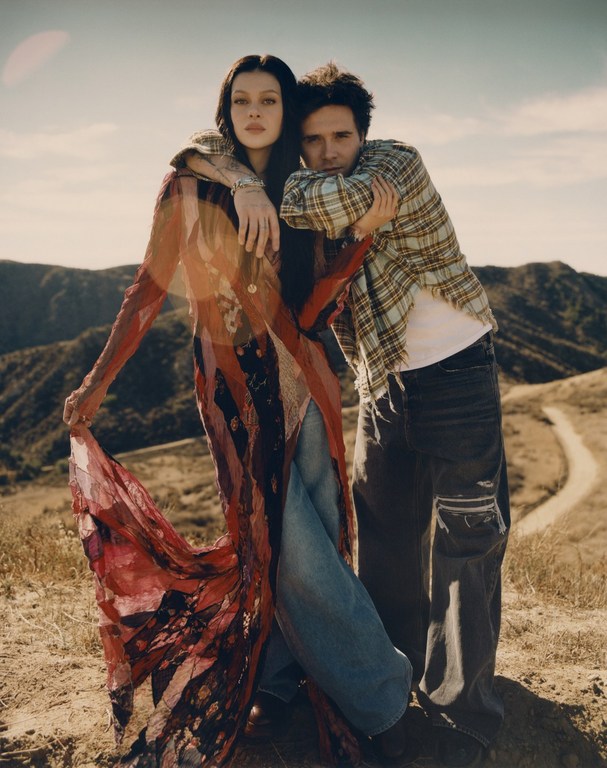 A stylish couple poses in a sun-drenched outdoor setting. The woman wears a flowing dress, while the man sports a casual plaid shirt.