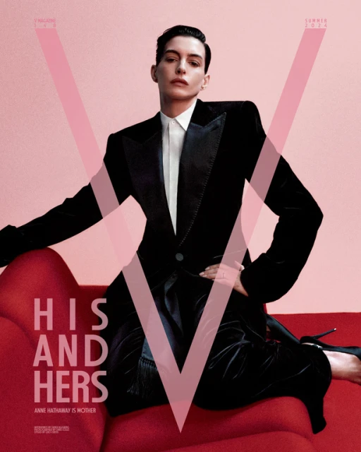 Anne Hathaway poses in a black velvet tuxedo jacket and pants on a red couch in a studio. Light pink background. Fashion magazine cover.