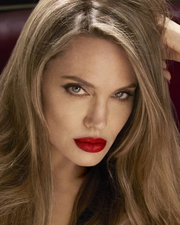 Close-up portrait of Angelina Jolie with long blonde hair, bold red lipstick, and defined eye makeup.