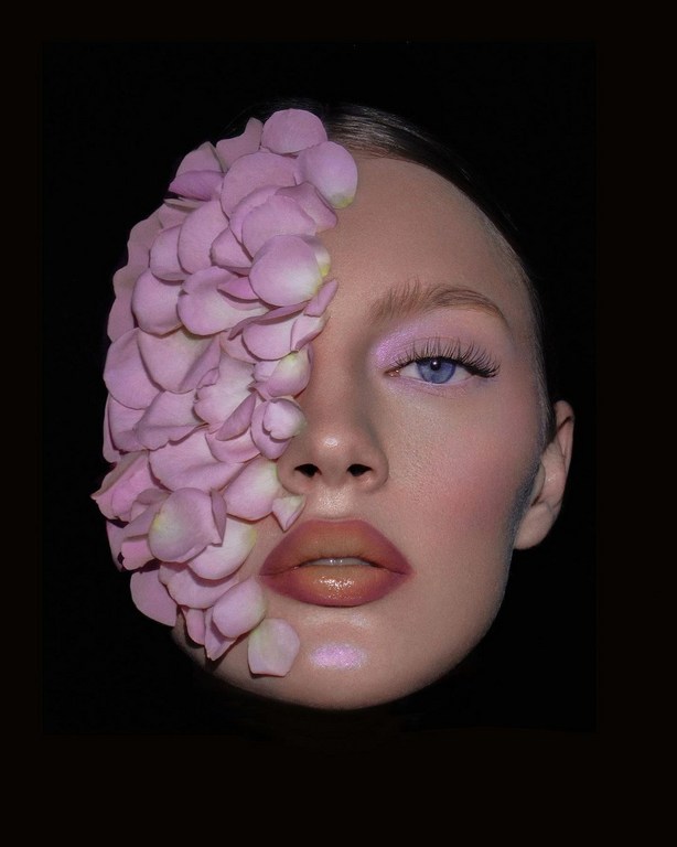 Close-up portrait of a woman with rose petals on one side of her face, set against a dark background, artistic makeup, and soft lighting.