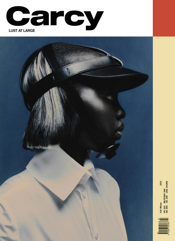 Magazine cover featuring a person in a leather hat and white collared shirt against a blue backdrop with white and orange accents.