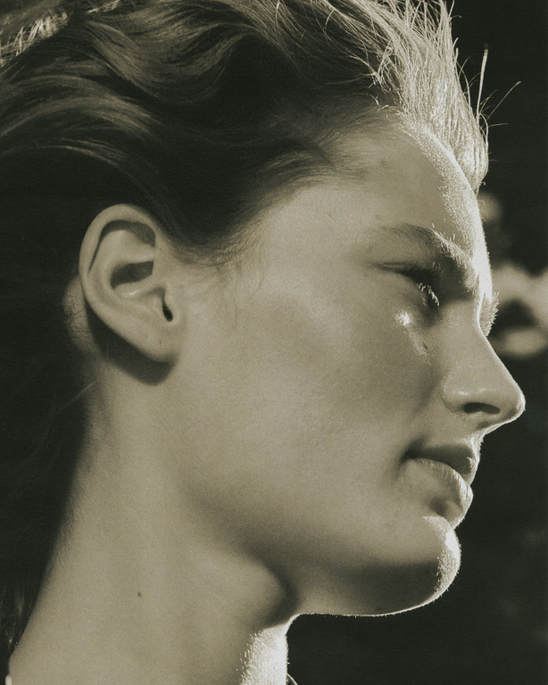 Close-up profile portrait of a woman with highlighted hair and natural skin texture against a dark background.