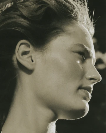 Close-up profile portrait of a woman with highlighted hair and natural skin texture against a dark background.