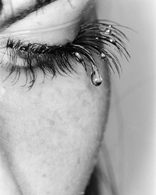 Close-up of an eye with long eyelashes and water droplets clinging to them, and one large tear falling.