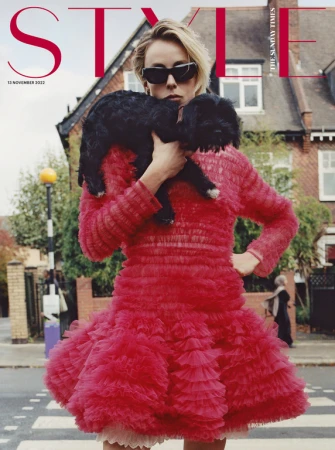 Magazine cover featuring a young woman in a red dress holding a black dog, standing on a crosswalk with houses in the background.