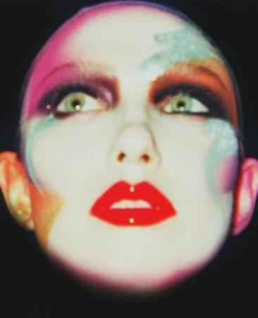 Close-up beauty portrait of a model with vibrant colorful makeup and bold red lips against a black background.