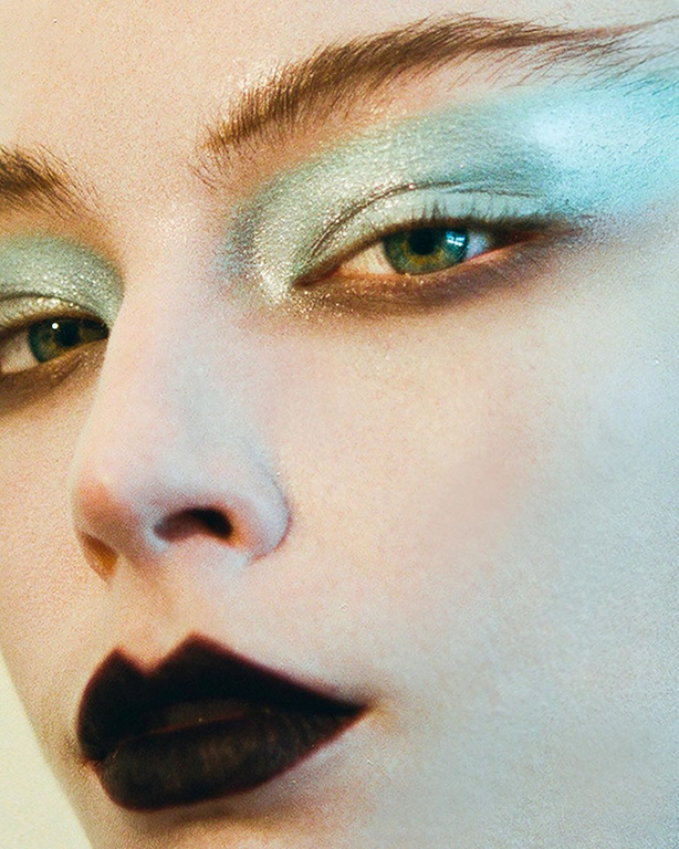 Close up beauty portrait of a woman with metallic pale green eyeshadow and dark brown lips.