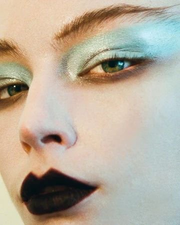 Close up beauty portrait of a woman with metallic pale green eyeshadow and dark brown lips.