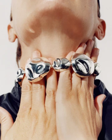 Close-up portrait of a person holding their hands to their neck wearing a large silver metallic sculptural necklace.
