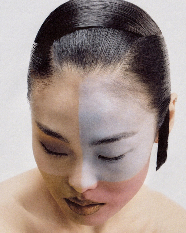 Asian woman with creative face makeup, shiny black hair, and closed eyes in a portrait-style photo taken in a bright photo studio.