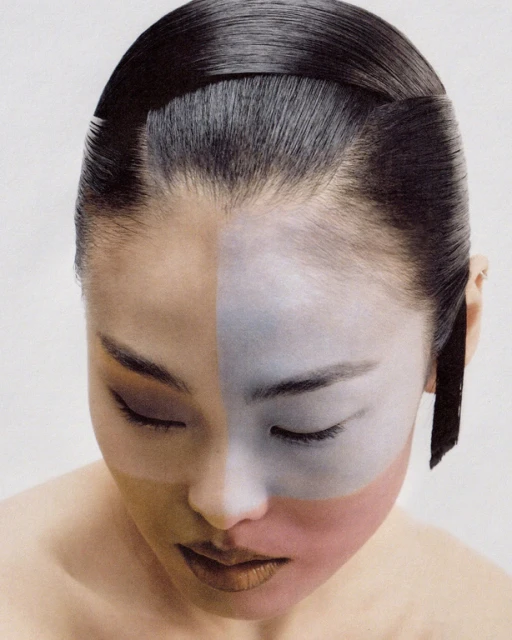 Asian woman with creative face makeup, shiny black hair, and closed eyes in a portrait-style photo taken in a bright photo studio.