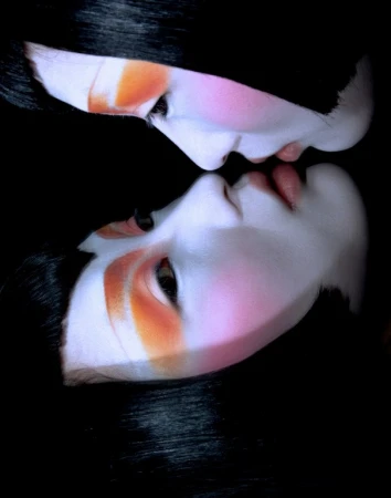 Close up portrait of two faces with pale complexions, dark hair, and striking orange and pink eye makeup reflected in a dark surface.