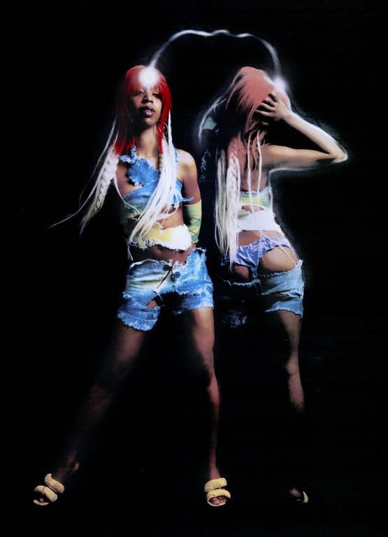 Two women with red hair and distressed denim pose in dark studio. They wear matching crop tops and chunky sandals. Post-production lighting effects.