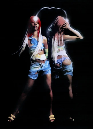Two women with red hair and distressed denim pose in dark studio. They wear matching crop tops and chunky sandals. Post-production lighting effects.