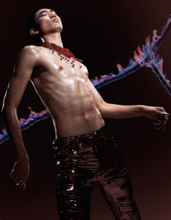 Artistic portrait of a shirtless person with red necklace and shiny pants, posing in a dark studio with artistic light effect.