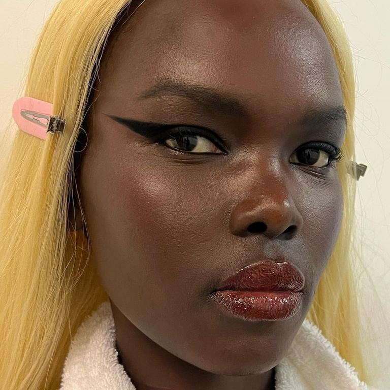 Close-up of a dark-skinned woman with blond hair, wearing black eyeliner and lip gloss, accessorized with hair clips, beauty shot.