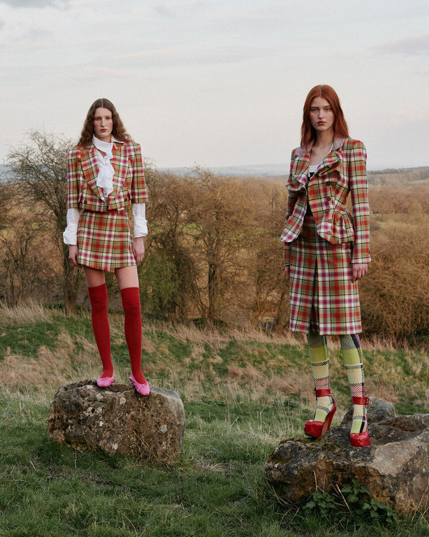 Two fashion models pose outdoors wearing matching plaid skirt suits with red platform heels and knee socks in a natural setting.
