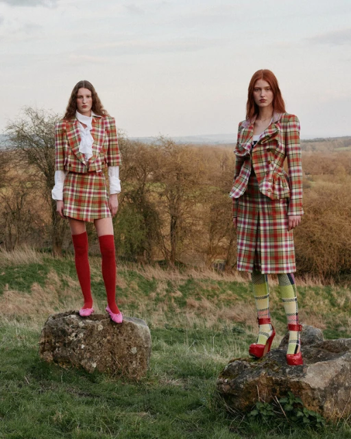 Two fashion models pose outdoors wearing matching plaid skirt suits with red platform heels and knee socks in a natural setting.