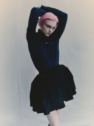 Model with pink hair wearing a dark turtleneck and flared skirt posed against a white studio seamless background