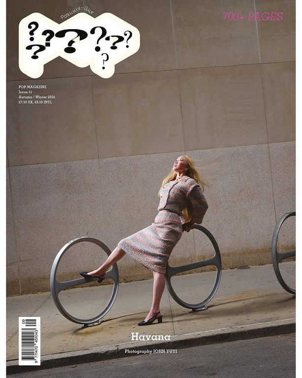 Magazine cover featuring a blonde woman in a skirt suit posing with a bike rack in an urban setting with muted, desaturated colors.