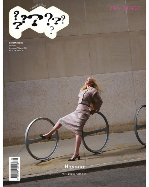 Magazine cover featuring a blonde woman in a skirt suit posing with a bike rack in an urban setting with muted, desaturated colors.