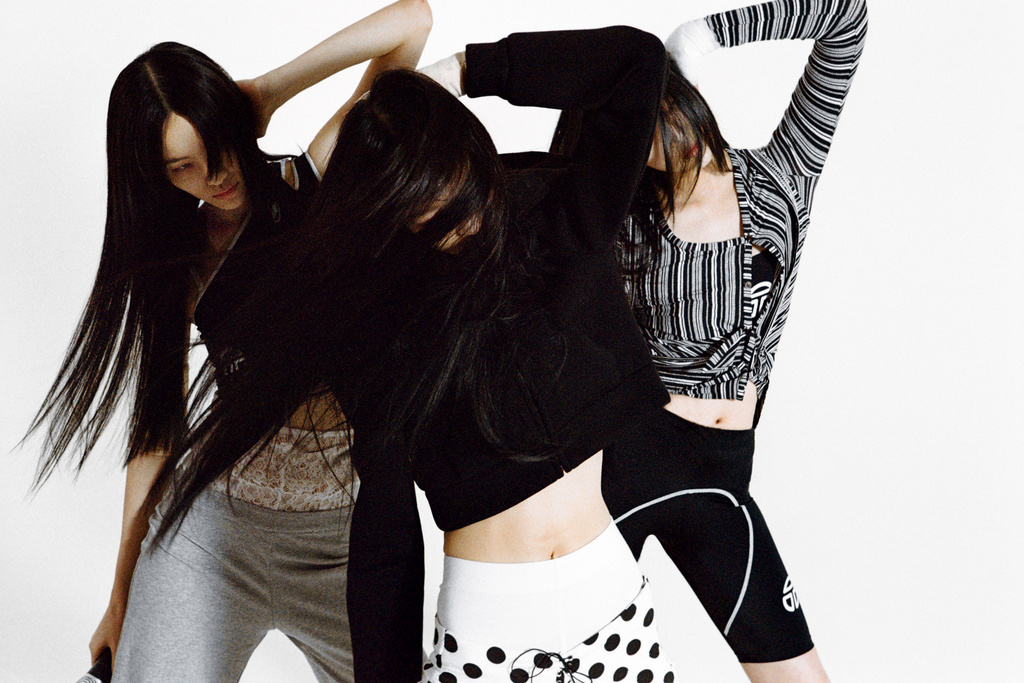 Three women in athletic wear strike a pose in a photo studio, the models are wearing monochrome tones of black, gray, and white.