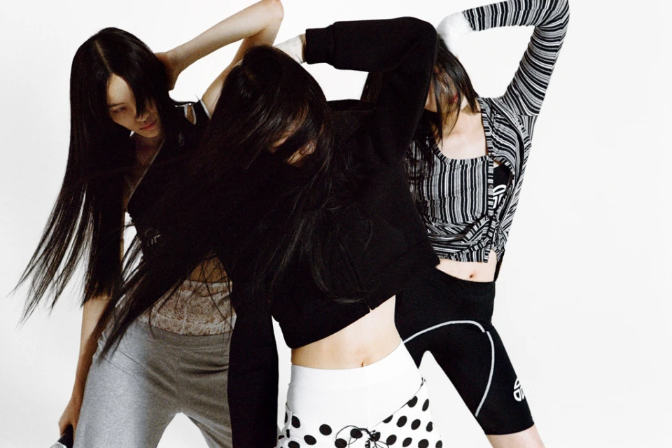 Three women in athletic wear strike a pose in a photo studio, the models are wearing monochrome tones of black, gray, and white.