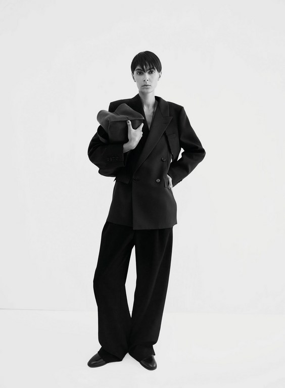 Model with short dark hair wearing an oversized black blazer and trousers against a white background