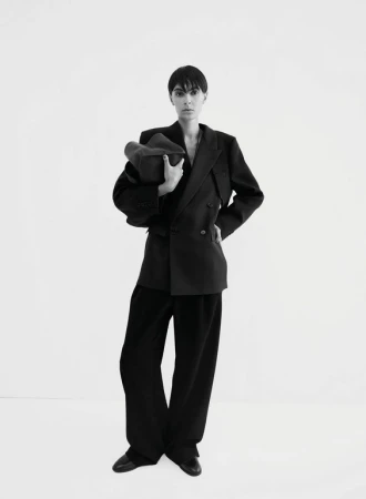 Model with short dark hair wearing an oversized black blazer and trousers against a white background