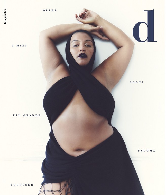 Paloma Elsesser poses for magazine cover, wearing black wrap dress and head covering against a neutral background.
