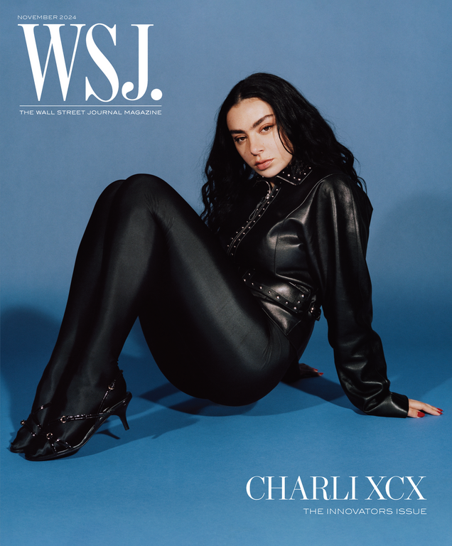 Charli XCX poses on a WSJ. Magazine cover, seated and looking at the camera in a black leather outfit against a blue background.