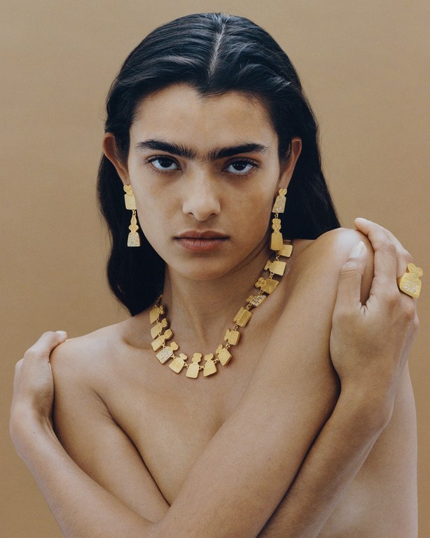 Portrait of a woman wearing statement gold jewellery and earrings against a neutral beige background