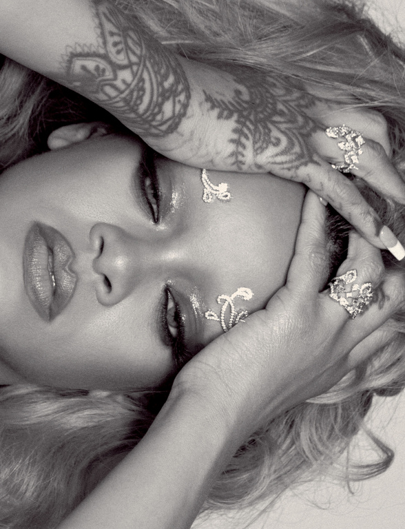Black and white portrait of a woman with closed eyes, hand tattoos, rings, and decorative makeup. Hair is blonde. Low angle shot.