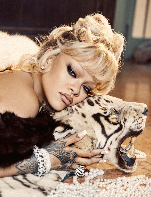 Close-up portrait of a fair-skinned woman with platinum blonde hair styled up, wearing heavy makeup, resting her head on a tiger prop.