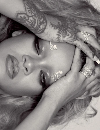 Close-up portrait of Rihanna with decorative eye jewels, ornate hand tattoos, and statement rings styled by Jackson Heller.