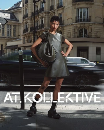 Model standing on a Parisian street holding a large dark leather bag, wearing a sleeveless leather dress and platform shoes.