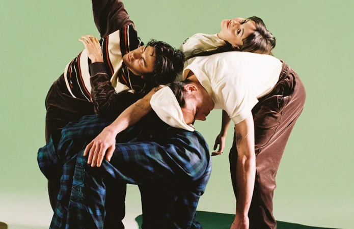 Four people in a coordinated pose wearing casual clothing against a solid green background, showcasing a modern and youthful aesthetic.