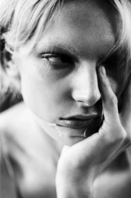 Monochrome portrait of a young adult woman with her hand touching her face in a close-up shot, capturing her pensive expression and delicate features.