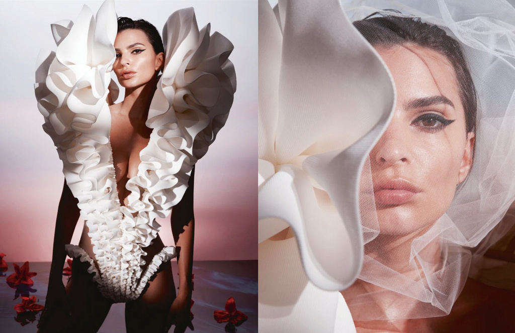 Portrait of an adult female fashion model wearing a white ruffle dress with red flowers in a photo studio against a pink background.