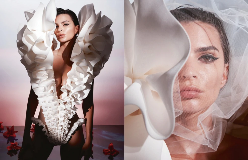 Portrait of an adult female fashion model wearing a white ruffle dress with red flowers in a photo studio against a pink background.