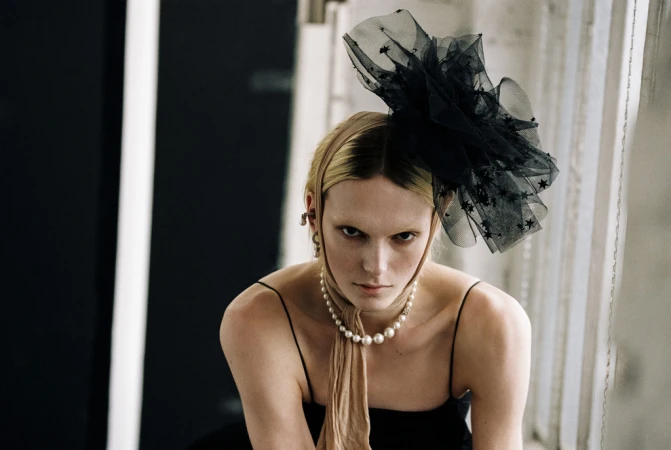 Striking studio portrait of a woman with blonde hair, adorned with a black star-studded headpiece and pearl necklace, gazing directly at the viewer.