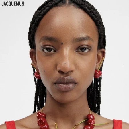 Close-up portrait of a Black woman wearing cherry-shaped earrings and a red cherry necklace with makeup by Yumiko Hikage.