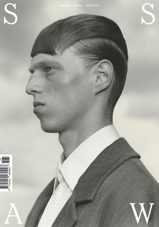 Monochromatic fashion editorial portrait of a man with a blunt haircut wearing a coat against a blurred sky background, magazine cover.