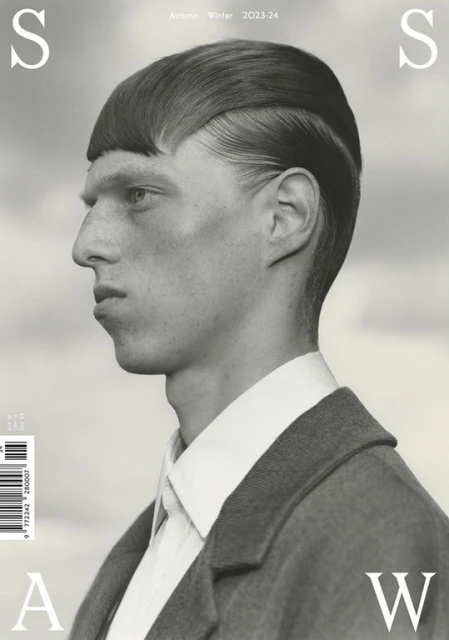 Monochromatic fashion editorial portrait of a man with a blunt haircut wearing a coat against a blurred sky background, magazine cover.
