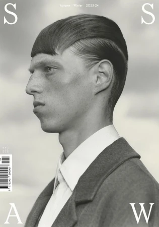 Monochromatic fashion editorial portrait of a man with a blunt haircut wearing a coat against a blurred sky background, magazine cover.