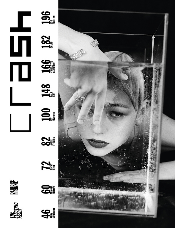 Black and white magazine cover featuring a woman's face partially submerged in water in a clear container, jewelry on hand and wrist.