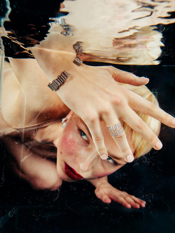 Underwater portrait of a woman with blonde hair and red lipstick wearing statement jewelry, including a ring and bracelet.